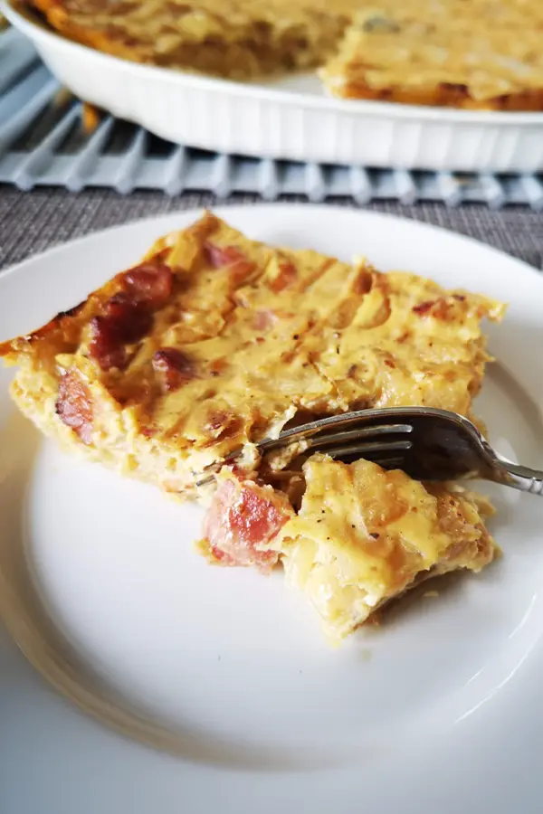 A slice of caramelized onion tart on a white plate with a fork cutting into it.