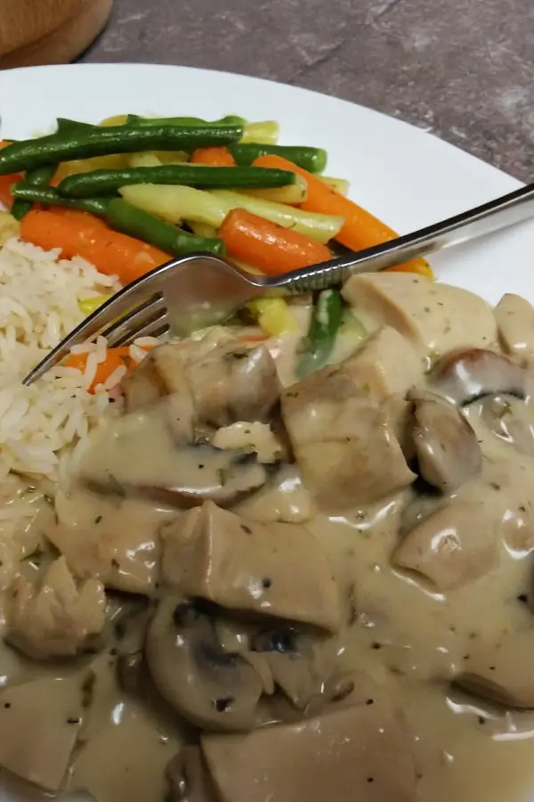 A plate with creamy chicken fricassee, rice, mixed vegetables, and a fork placed on top.