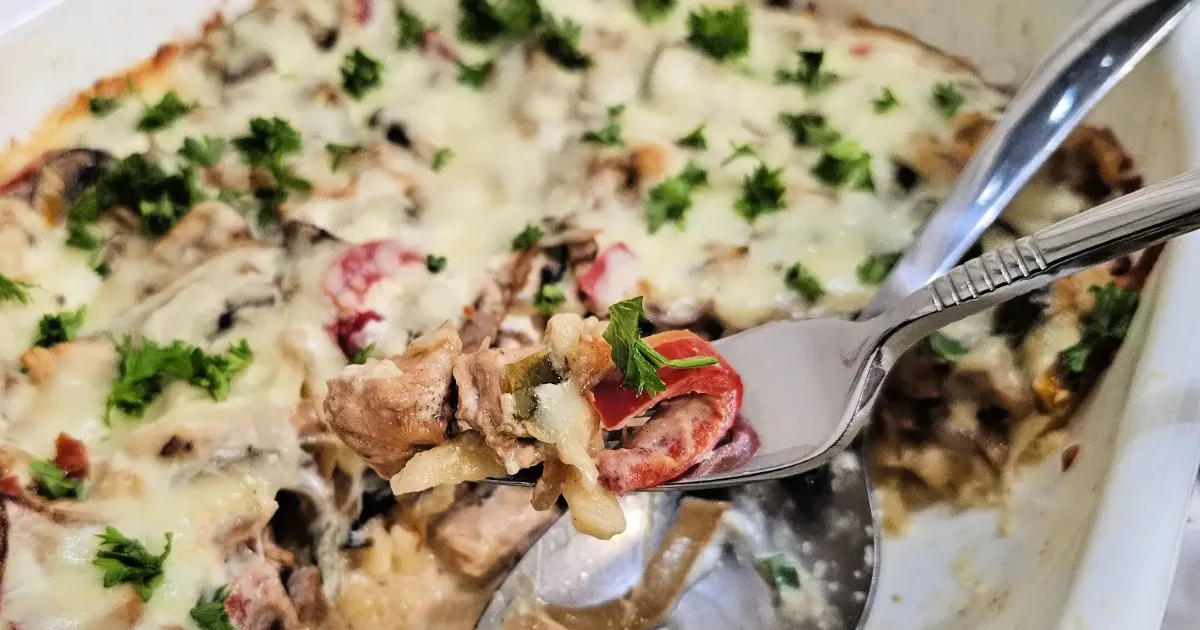 Forkful of chicken spätzle casserole lifted from the baking dish, showing creamy cheese and mushrooms