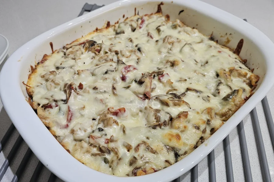Baked chicken spätzle casserole in a white dish with melted cheese, mushrooms and red peppers browned at the edges