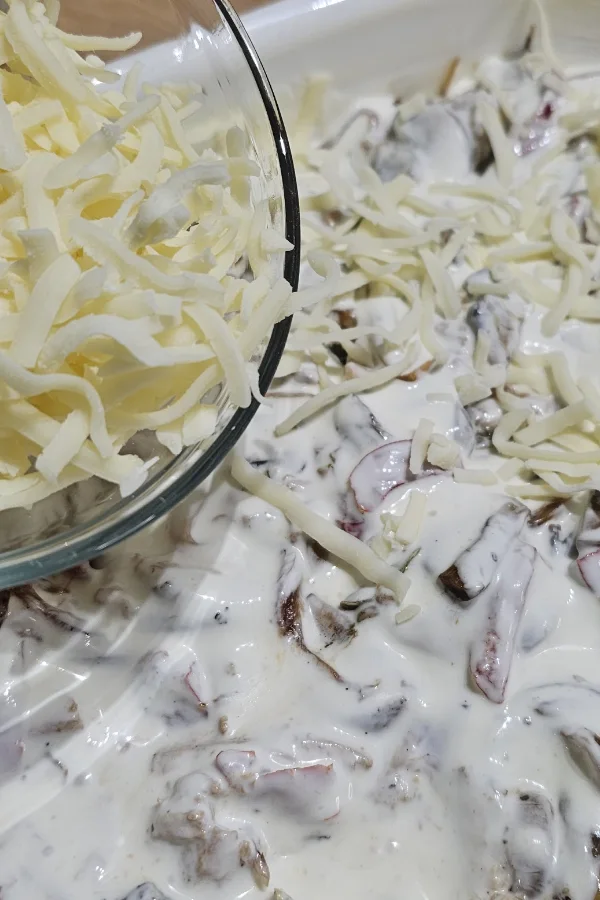 Shredded cheese scattered over creamy chicken spätzle casserole before baking