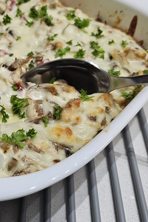 Serving spoon scooping creamy chicken spätzle casserole topped with melted cheese and fresh parsley