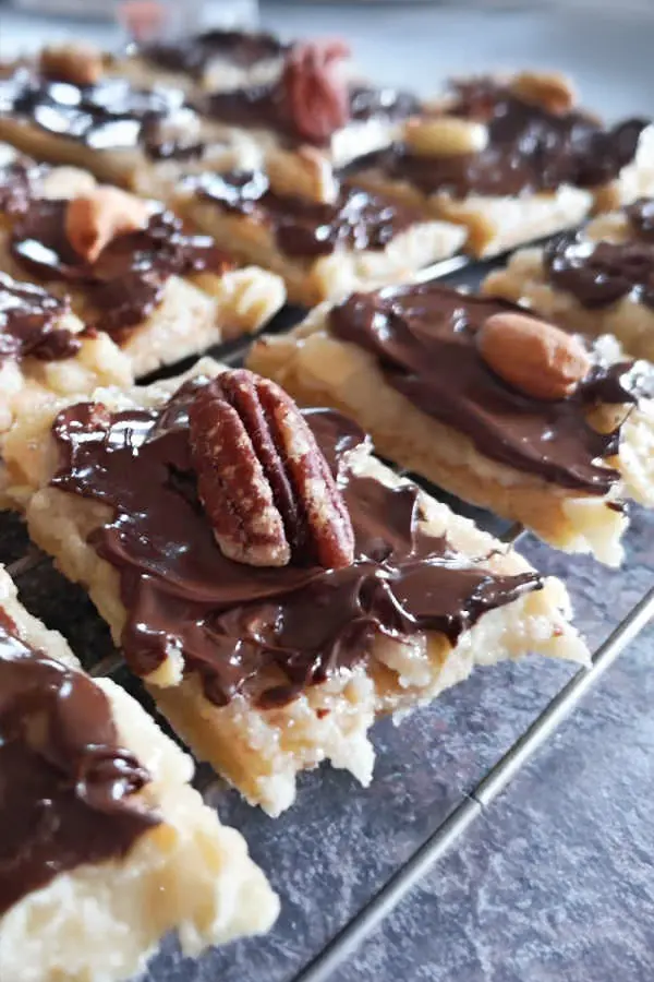 Rectangular pecan bars topped with melted chocolate and pecan nuts on a dark surface.