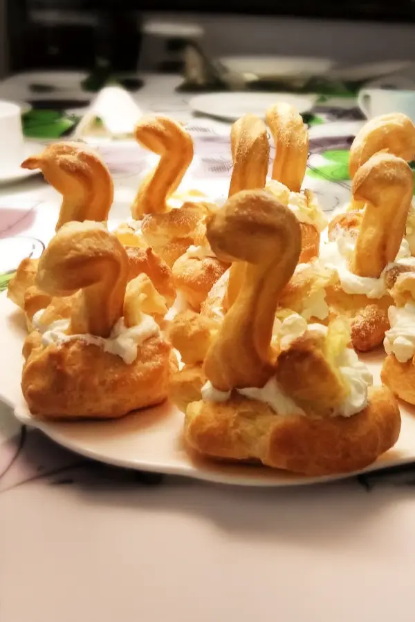 Plate of cream puffs shaped like swans with pastry necks and whipped cream on a table.