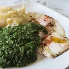 Plate of creamed spinach served with mashed potatoes and two fried eggs, showing the creamy texture and vibrant green color of the spinach.