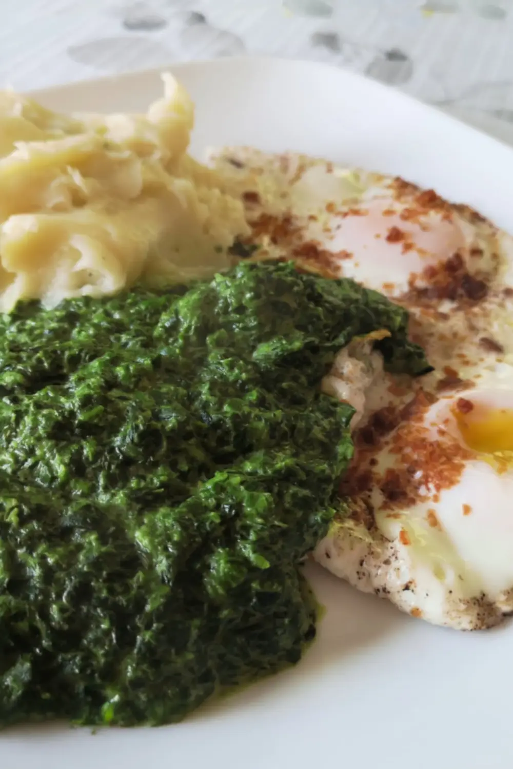 Plate of creamed spinach served with mashed potatoes and two fried eggs, showing the creamy texture and vibrant green color of the spinach.