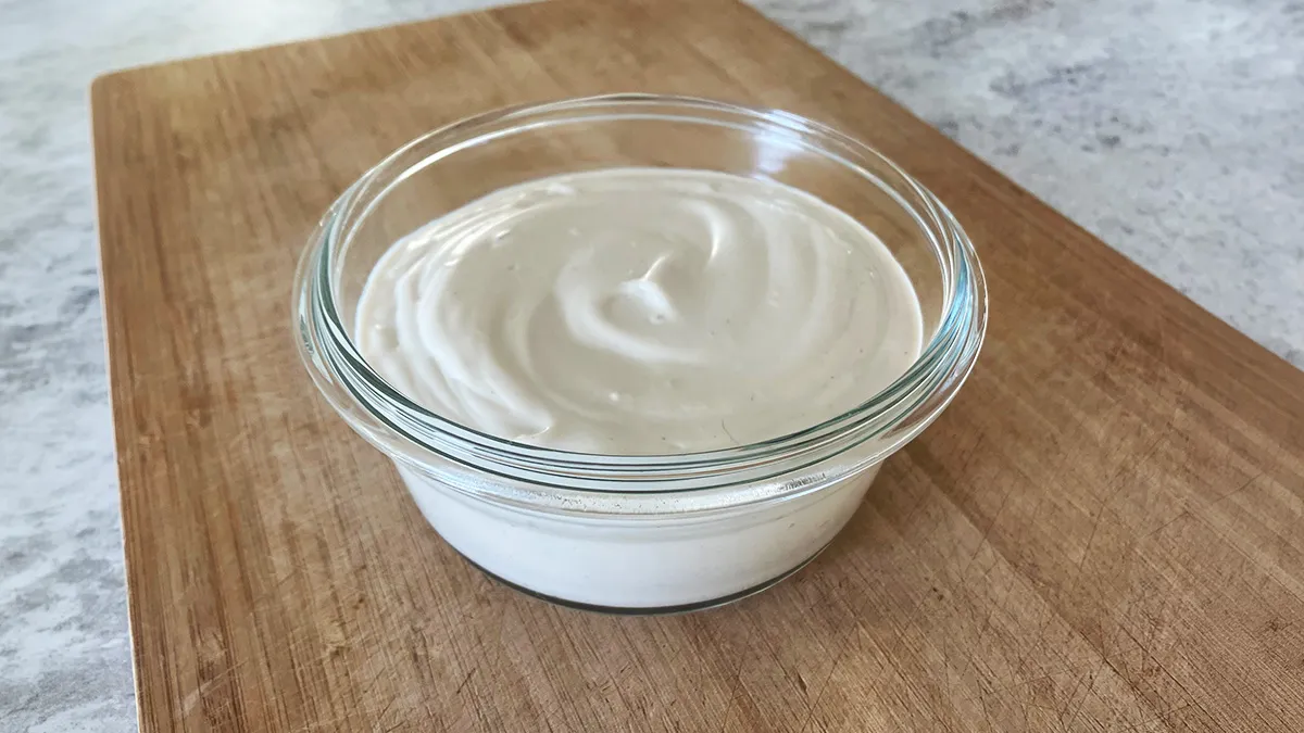 Bowl of thick dairy-free sour cream on a wooden board, smooth and creamy.