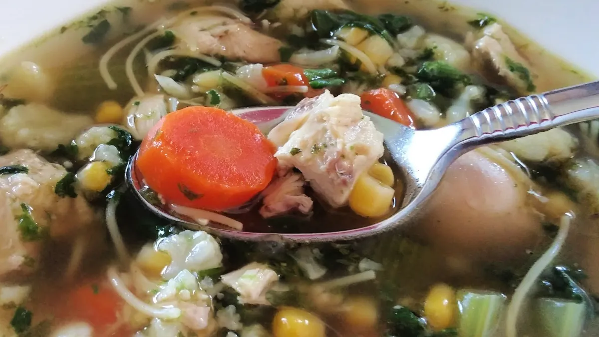 Homemade chicken noodle soup with carrots, celery, corn, cauliflower, and tender chicken in a clear broth.