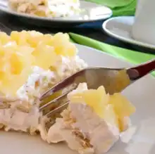 A fork cutting into a slice of whipped cream and pineapple-topped icebox cake.