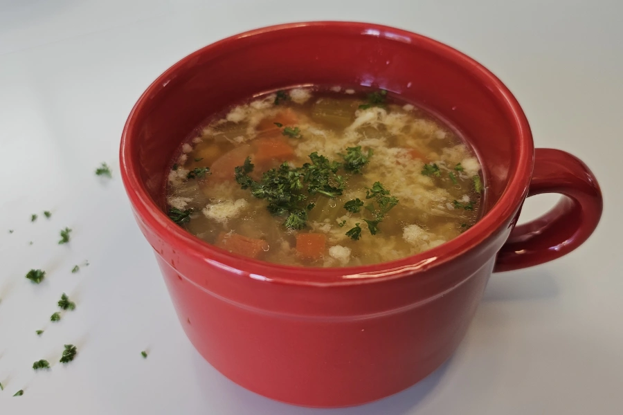 German egg drop soup in a red bowl with scattered parsley