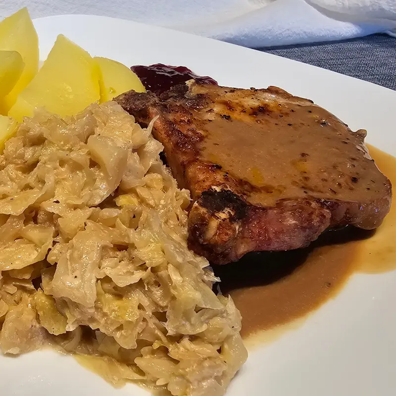 Plate of German creamed cabbage served with pork chop, gravy, and boiled potatoes. Plate of German creamed cabbage served with pork chop, gravy, and boiled potatoes.