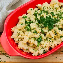 Red Bowl of German egg noodles sprinkled with fresh parsley.
