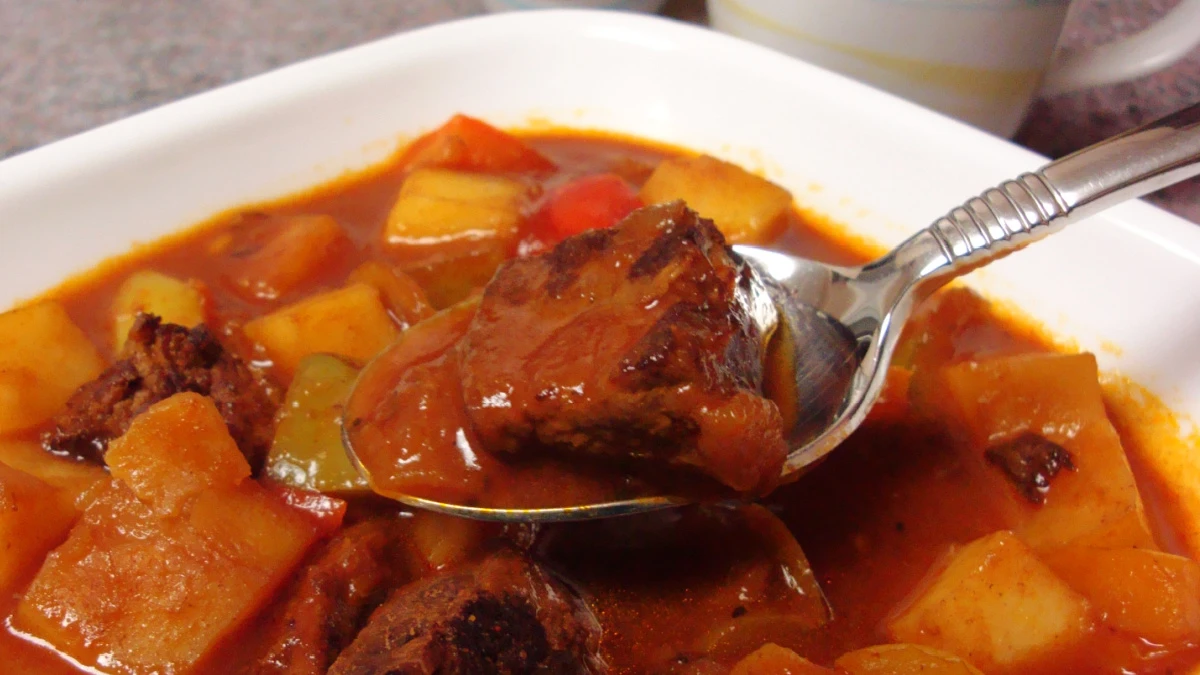 Spoonful of German goulash stew with tender beef chunks, potatoes, and peppers in a rich paprika tomato sauce