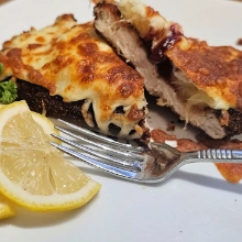 Close-up of Hawaiian chicken schnitzel cut open to show cranberry sauce and melted cheese, with a fork and lemon wedge