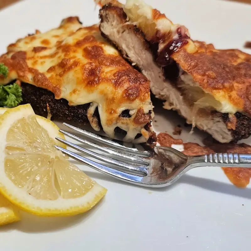 Close-up of Hawaiian chicken schnitzel cut open to show cranberry sauce and melted cheese, with a fork and lemon wedge