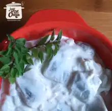 Creamy herring salad garnished with parsley in a red bowl.