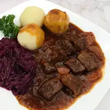 Plate of beef goulash with red cabbage and potato dumplings.