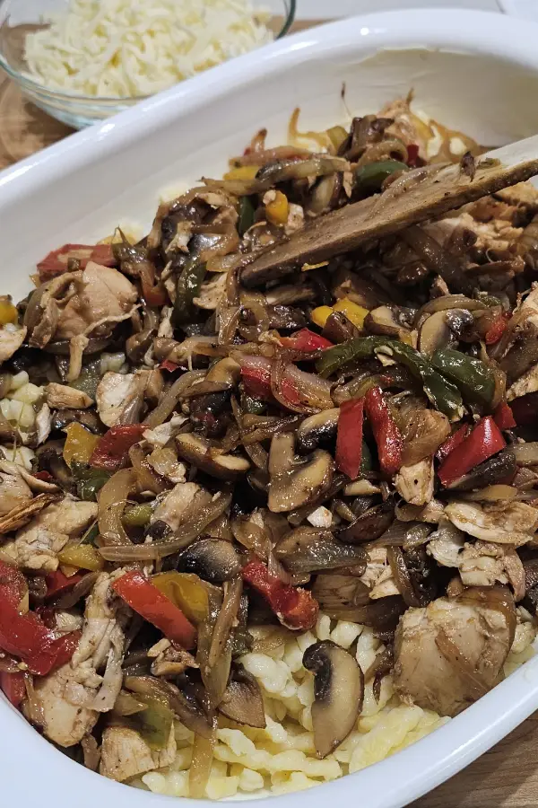 Chicken, mushroom and pepper mixture spread over cooked spätzle in a white casserole dish