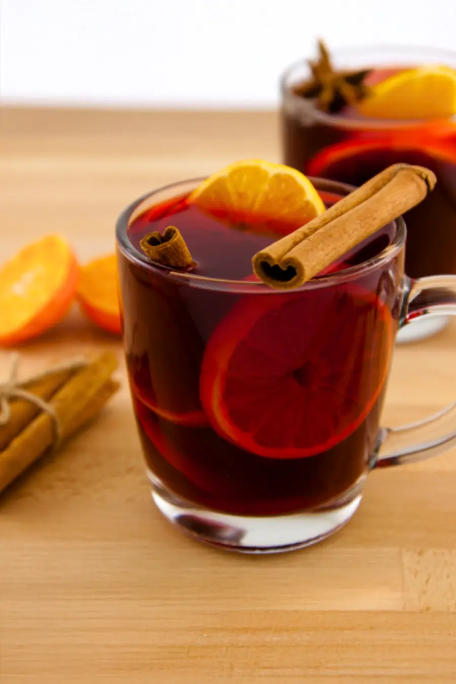 Glass mug of mulled wine with orange slices and a cinnamon stick on a wooden table.