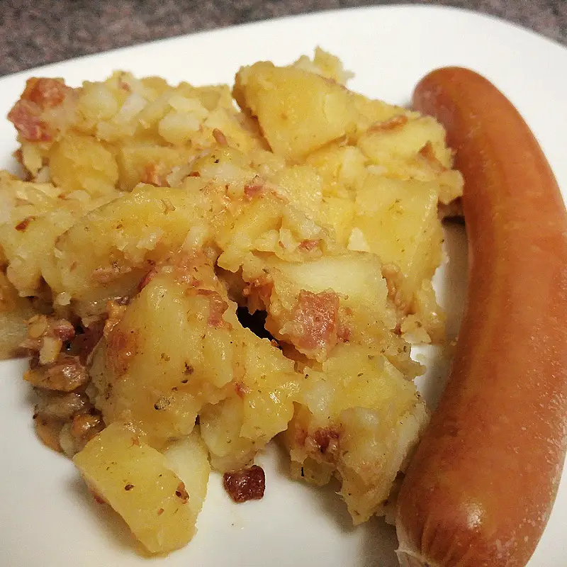 Southern German potato salad with bacon served beside a sausage