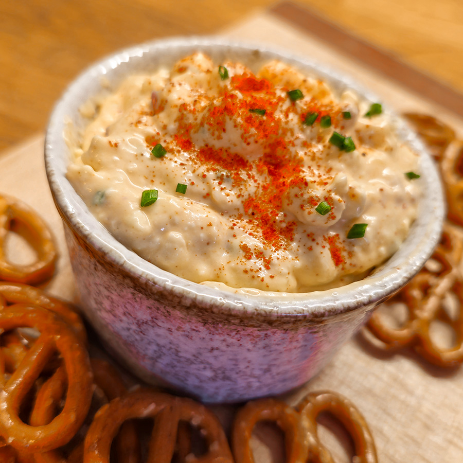 Bowl of Obatzda cheese spread topped with paprika and chives, served with pretzels.