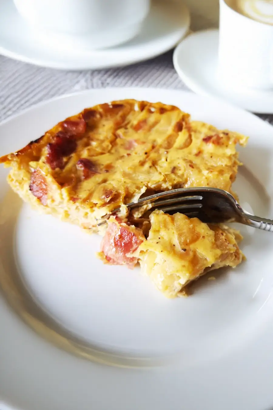 A slice of onion tart with visible chunks of onion and bacon on a white plate, with a fork resting on the slice.