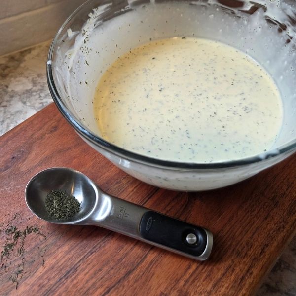 Creamy dill pickle pasta salad dressing in glass bowl with dill seasoning