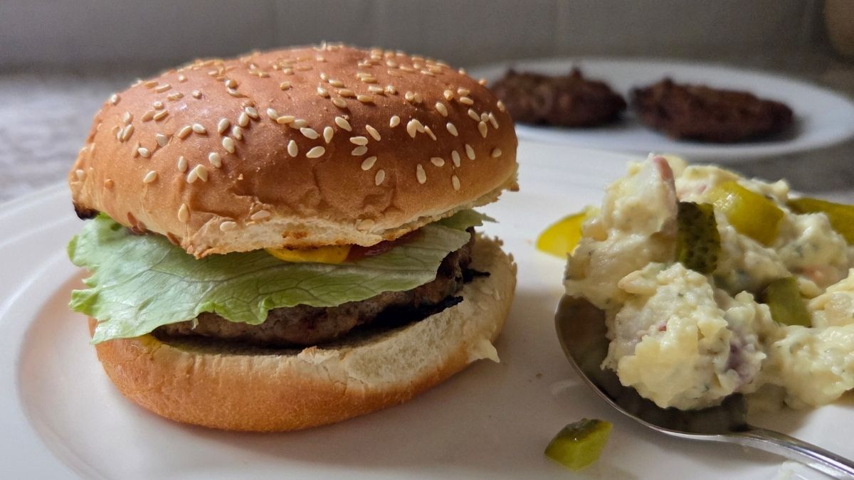 Pickle stuffed burgers on a white plate with German potato salad