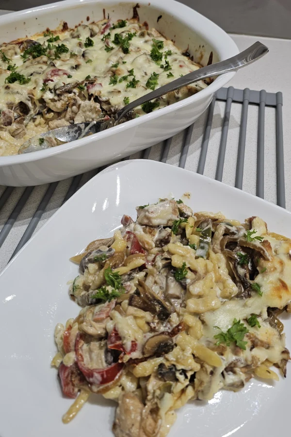 Serving spoon scooping creamy chicken spätzle casserole topped with melted cheese and fresh parsley