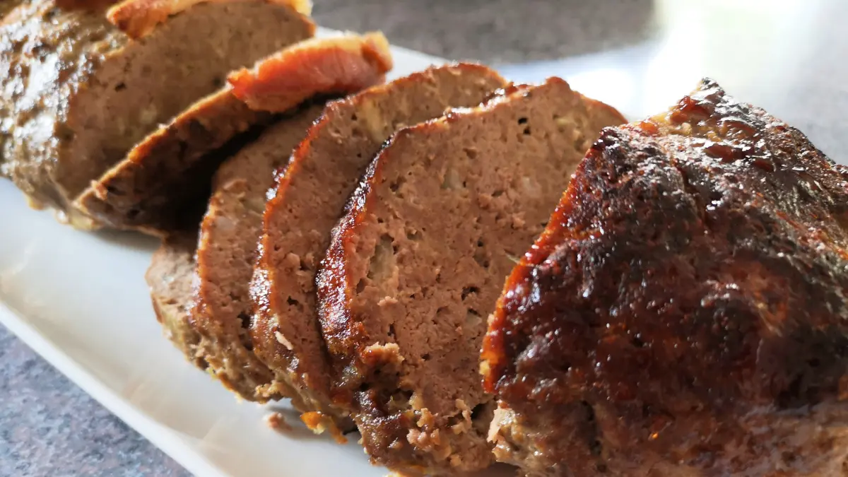 Close-up of juicy, sliced German meatloaf on a white serving plate.
