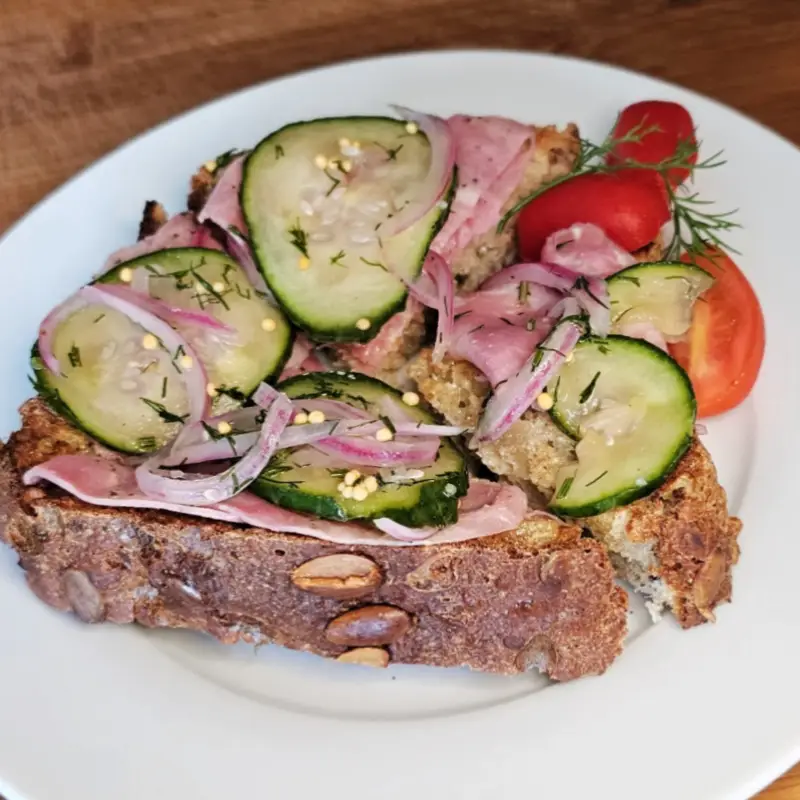 Open-faced ham sandwich topped with German refrigerator pickles and served with cherry tomatoes
