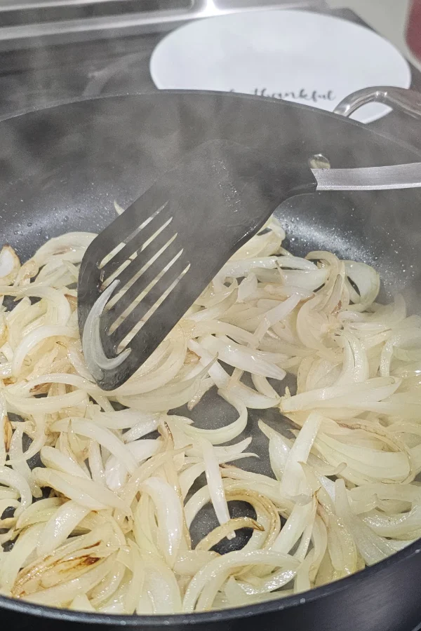 Sliced onions softening in a skillet with a slotted spatula
