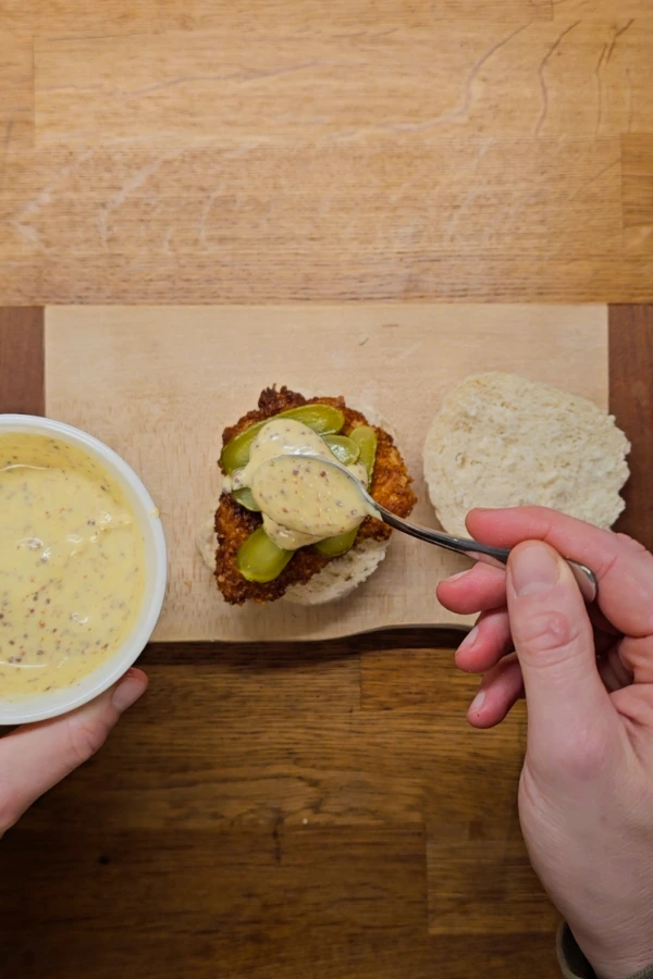 Assembling the schnitzel slider Assembling a pork schnitzel slider with sliced pickles and homemade beer mustard sauce on a toasted bun.
