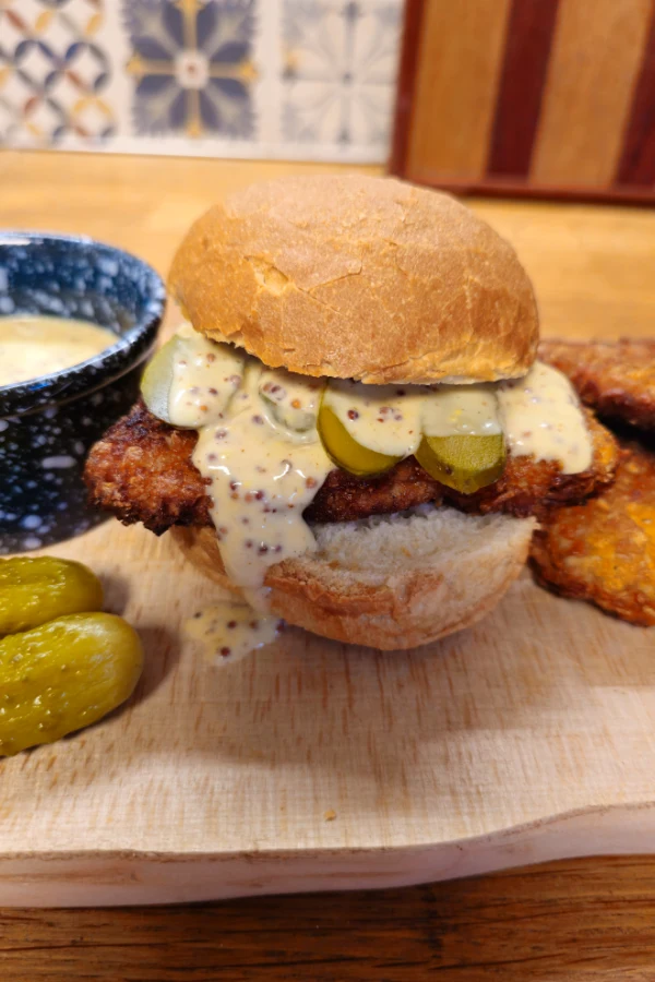 Finished pork schnitzel slider Pork schnitzel slider on a crusty roll topped with creamy beer mustard sauce and sliced pickles, served with extra sauce and mini pickles.