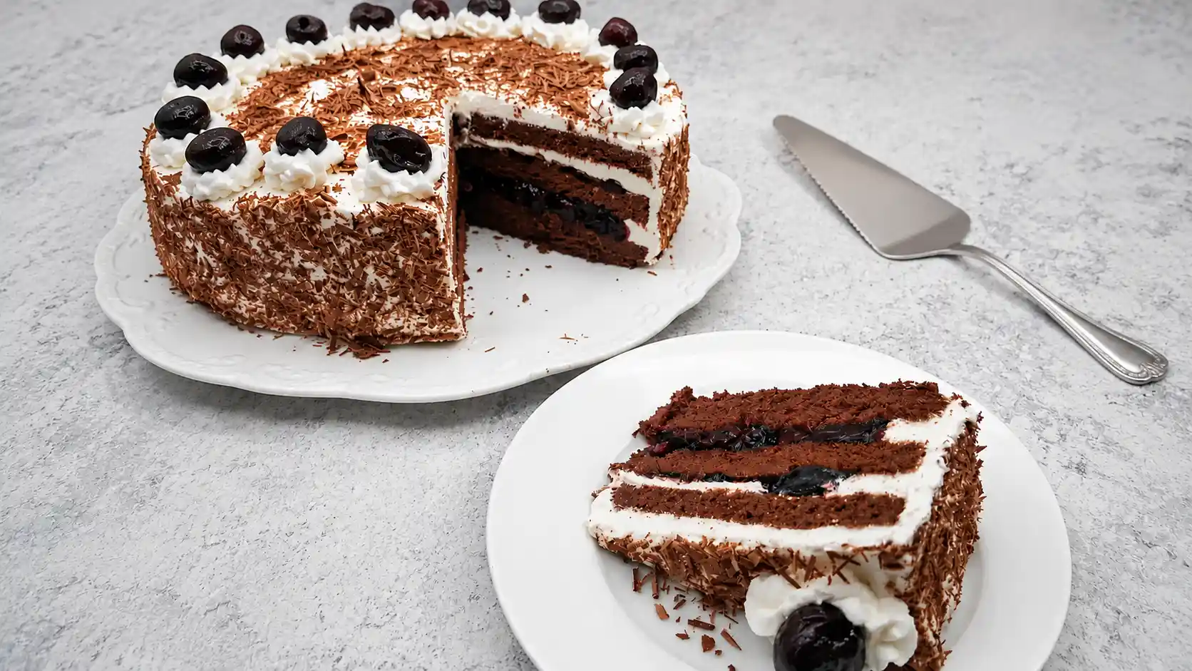 slice of traditional black forest cake on white plate with whole black forest cake in background