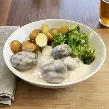 Vegan seitan meatballs in creamy sauce served with baby potatoes and broccoli on a white plate.