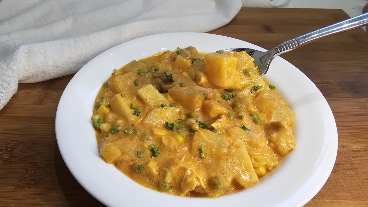 German party soup (ofensuppe) with chicken, potatoes, peas and corn in a creamy curry sauce, in a white bowl with a spoon