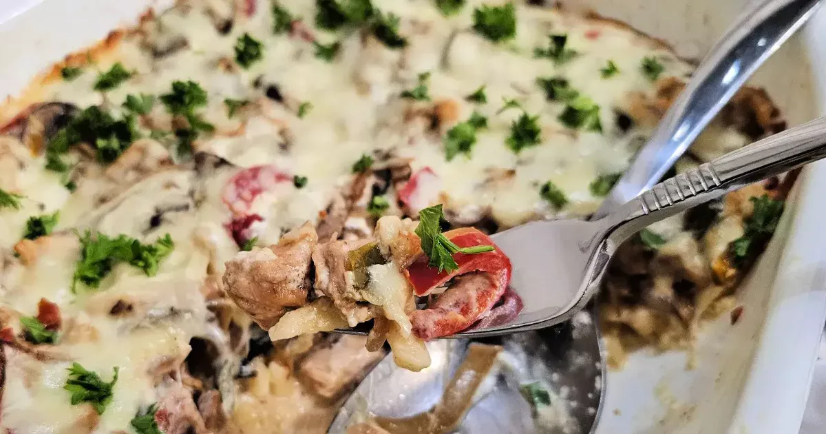 Forkful of chicken spätzle casserole lifted from the baking dish, showing creamy cheese and mushrooms