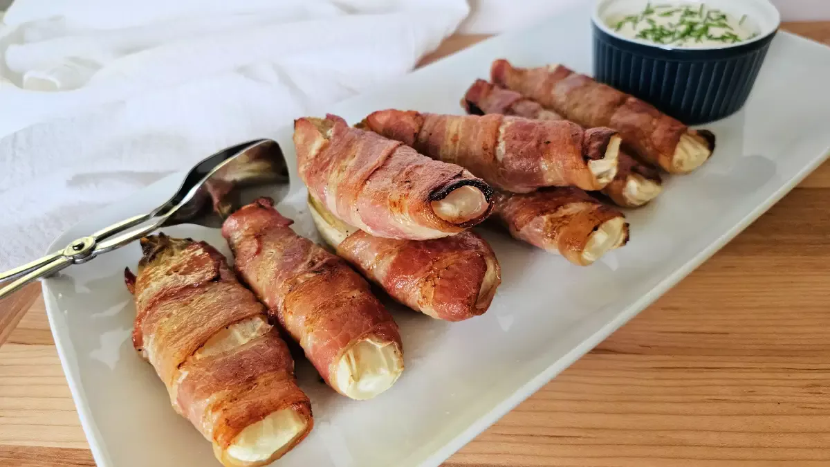 Bacon-wrapped Belgian endive served on a white platter with creamy mustard sauce and chives.