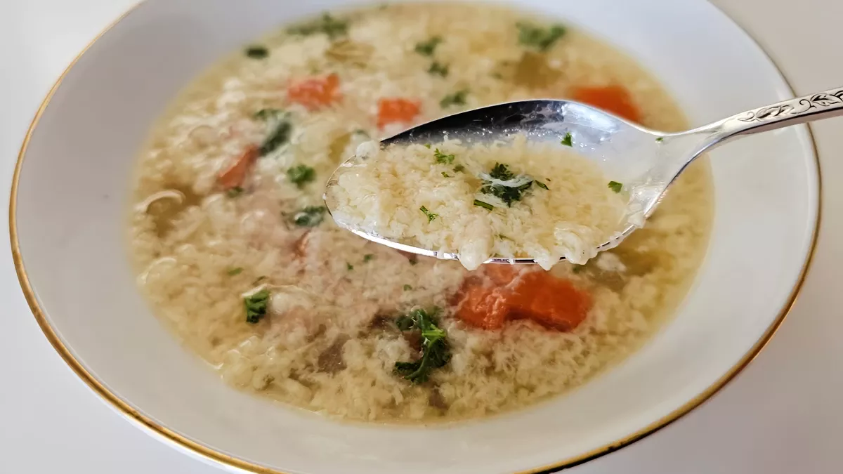 German egg drop soup (Einlaufsuppe) in a bowl with egg wisps, carrots, and herbs, shown on a spoon
