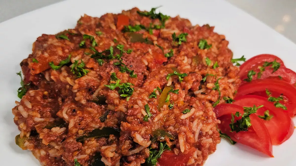 German rice dish with corned beef, peppers, and tomato sauce, garnished with parsley and served with sliced tomatoes.