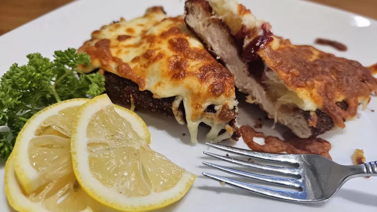 Hawaiian chicken schnitzel cut in half, showing chicken, cranberry sauce and broiled cheese on a white plate