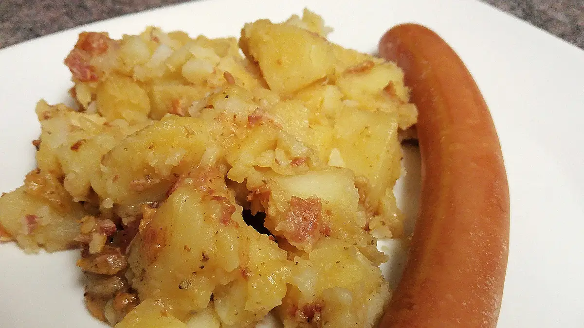 Southern German potato salad with bacon served beside a sausage