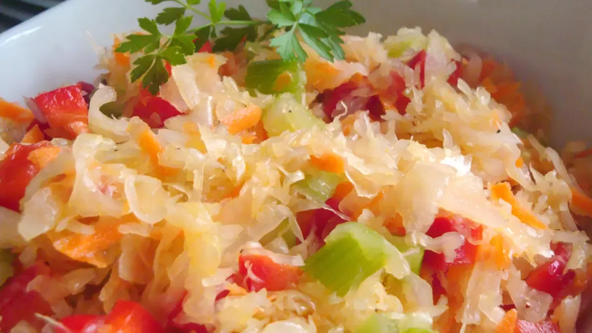 Close-up of colorful sauerkraut salad with shredded carrots, red peppers, celery, and fresh parsley garnish in a white dish.