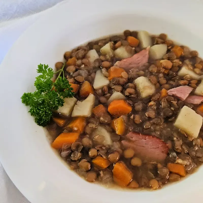 Hearty German lentil soup (Linsensuppe) with carrots, potatoes, smoked ham, and parsley, served in a white bowl